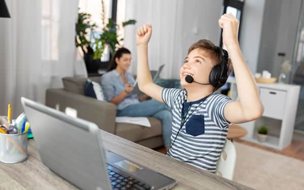 A kid celebrating at his laptop while a parent relaxes in the background
